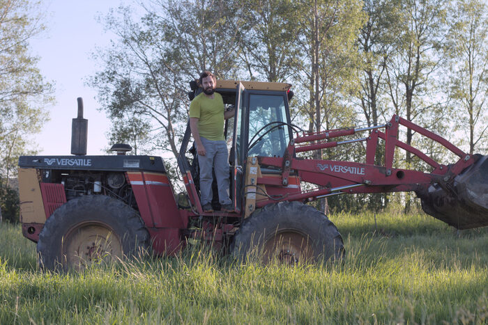 Standing in the open cab of a red Versatile tractor in the pasture, loader raised