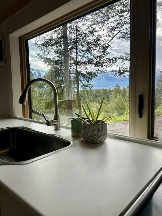 The kitchen run in the tiny house &mdash; a long counter, white cabinets, and the window bench at the far end